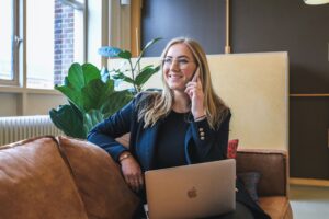 A blonde lady on the phone with a computer and a couch to represent lead generation.