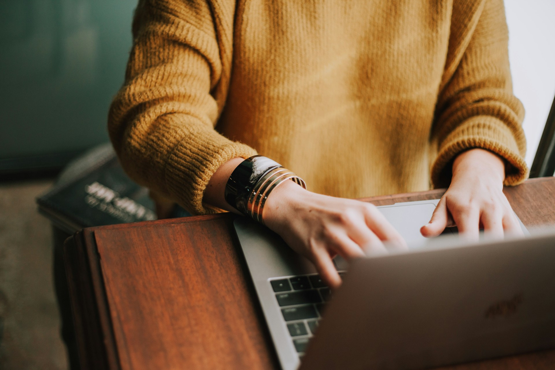 A person in a yellow sweater working on a macbook to represent a digital marketing agency job